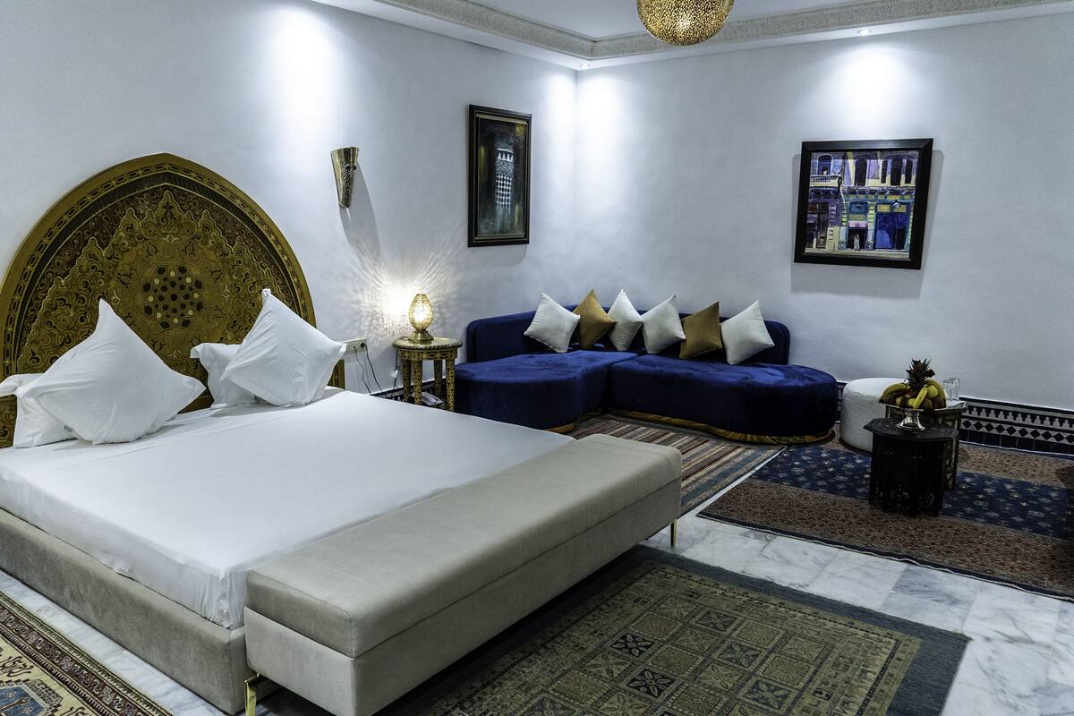 A modern hotel room with a large bed, a blue sofa, and a small table with fruit.