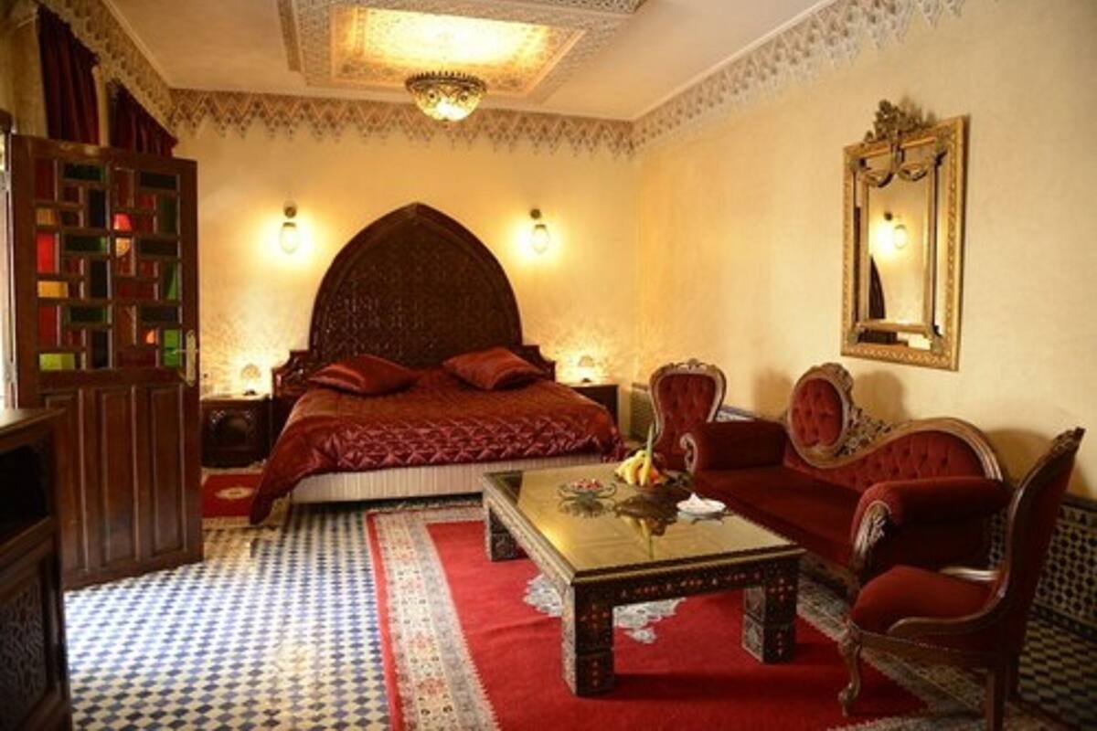 A traditional Moroccan room with a bed, a sofa, a coffee table, and a bookshelf.