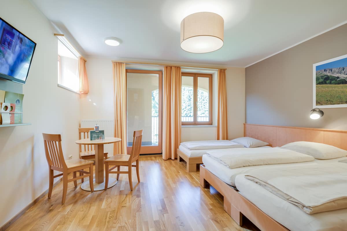 Een hotelkamer met een houten vloer, een eettafel met stoelen, een televisie, twee bedden en een raam met gordijnen.