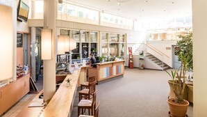 Un espace intérieur vaste et bien éclairé, avec un long comptoir en bois, plusieurs chaises en bois et un escalier menant à un niveau supérieur.