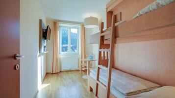 Un dormitorio con una cama litera, una mesita con una silla, una ventana con cortinas y un radiador.