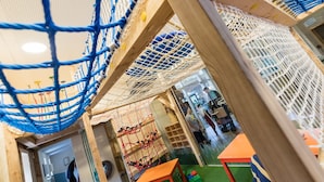 Un espace de jeux avec des structures d’escalade en filet et des tables de jeux en bois.