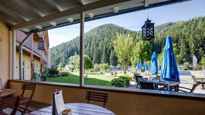Une terrasse avec des tables et des chaises en bois, une vue sur une montagne boisée et des parasols bleus.