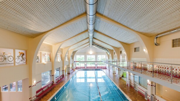Une piscine intérieure dotée d’un plafond haut, de grandes fenêtres et d’un sol carrelé.
