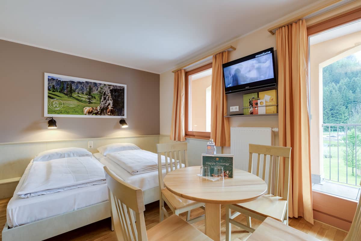 Een hotelkamer met twee eenpersoonsbedden, een televisie aan de muur, een tafel met stoelen en een raam met gordijnen.