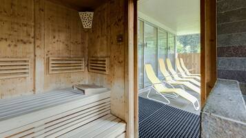 Una sauna con paredes de madera, un banco y una puerta de vidrio que da a un área de descanso exterior con sillones.