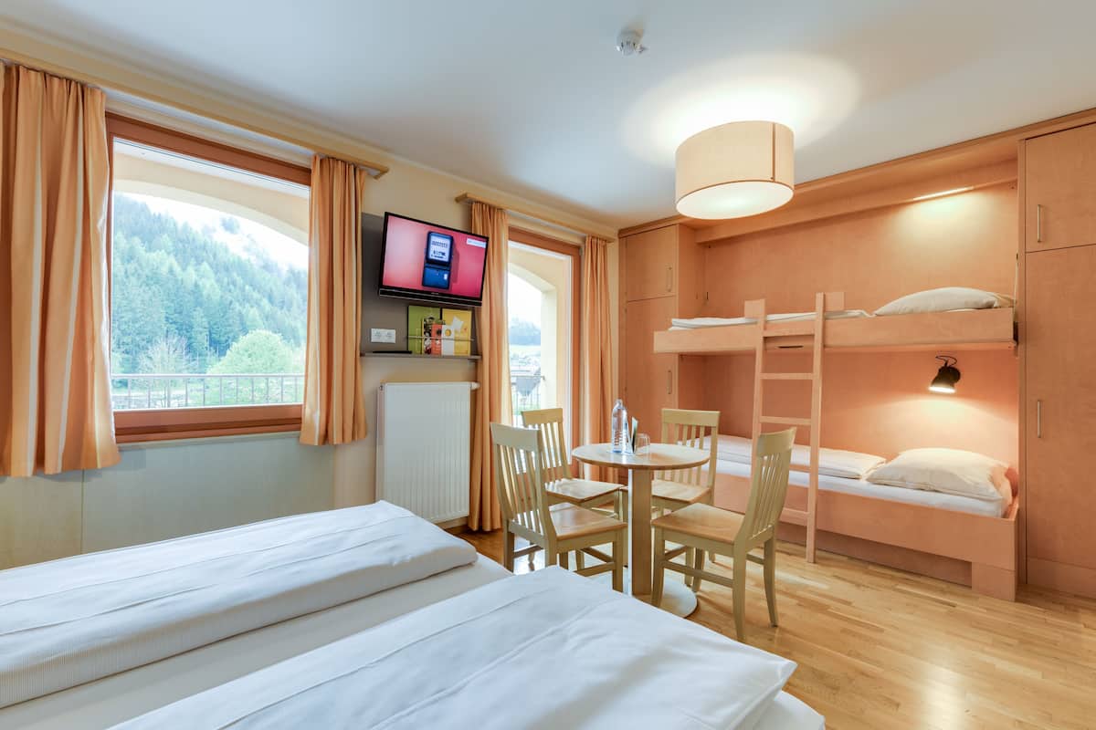 Een hotelkamer met een bed, een bureau met stoel, een televisie en een stapelbed.