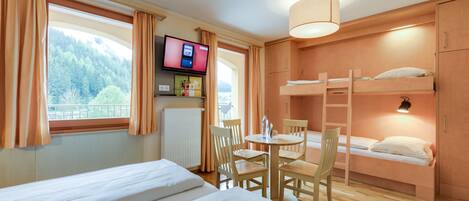 A hotel room with a bed, a desk with a chair, a TV, and a bunk bed.