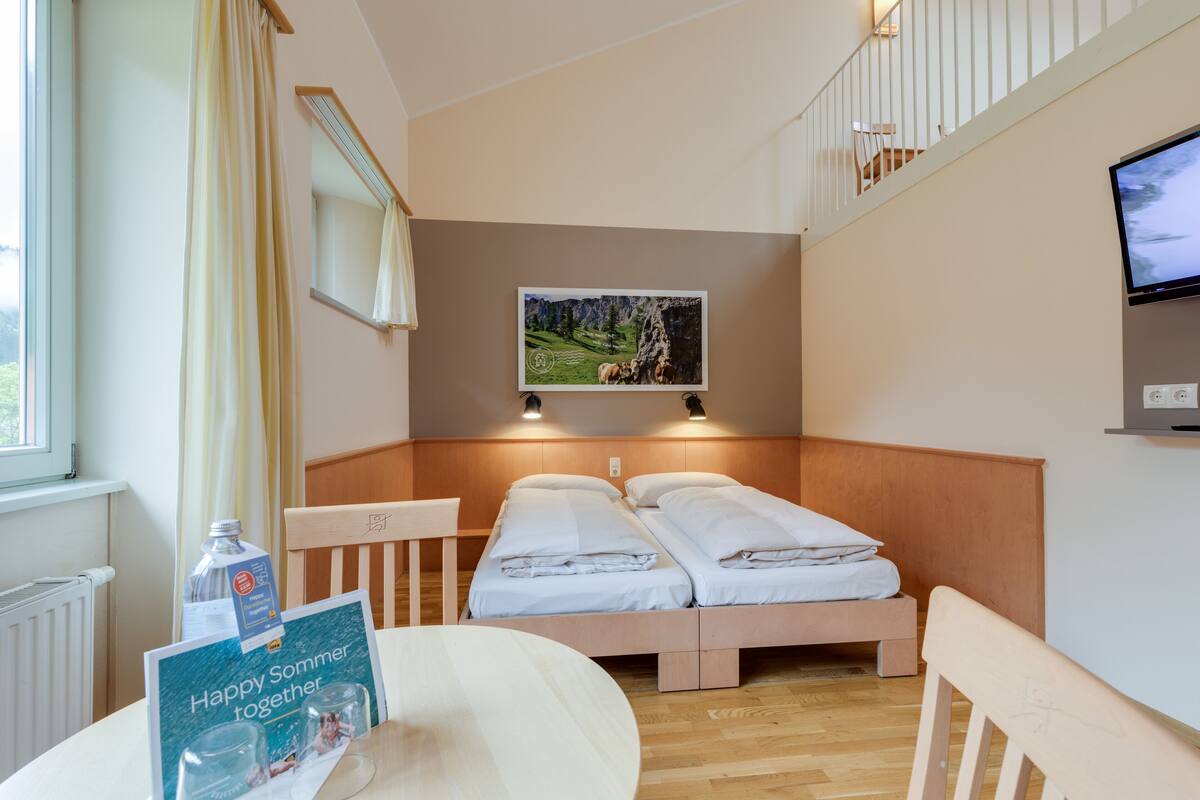 Hotelkamer met twee bedden, een televisie, een tafel met een fles en kaart, en een raam met gordijnen.