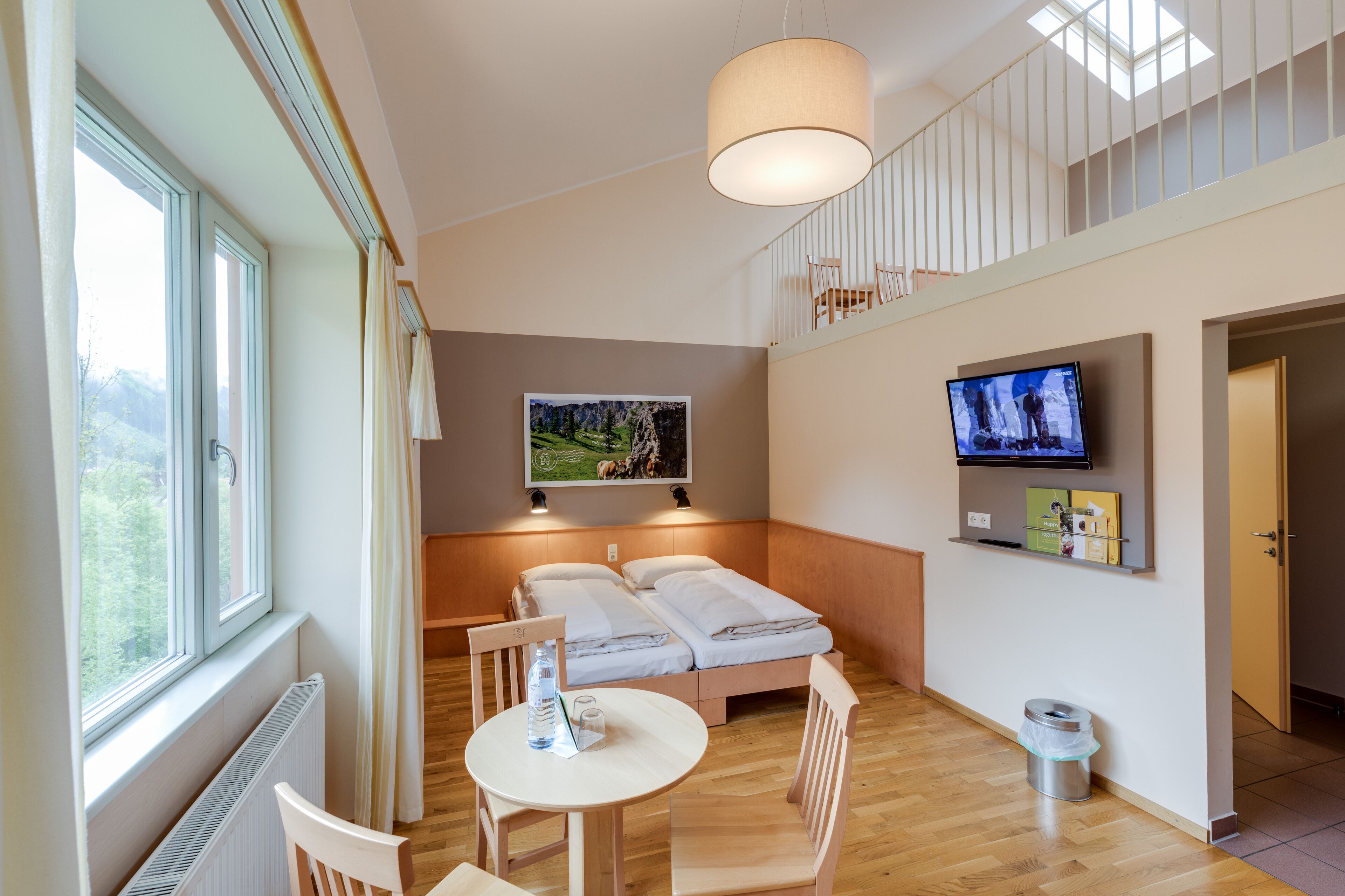 A hotel room with a bed, a TV, a painting, a window, and a table with chairs.
