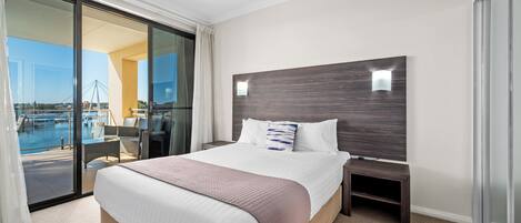 A hotel room with a large bed, a nightstand, a glass door leading to a balcony with a view of a bridge and water.