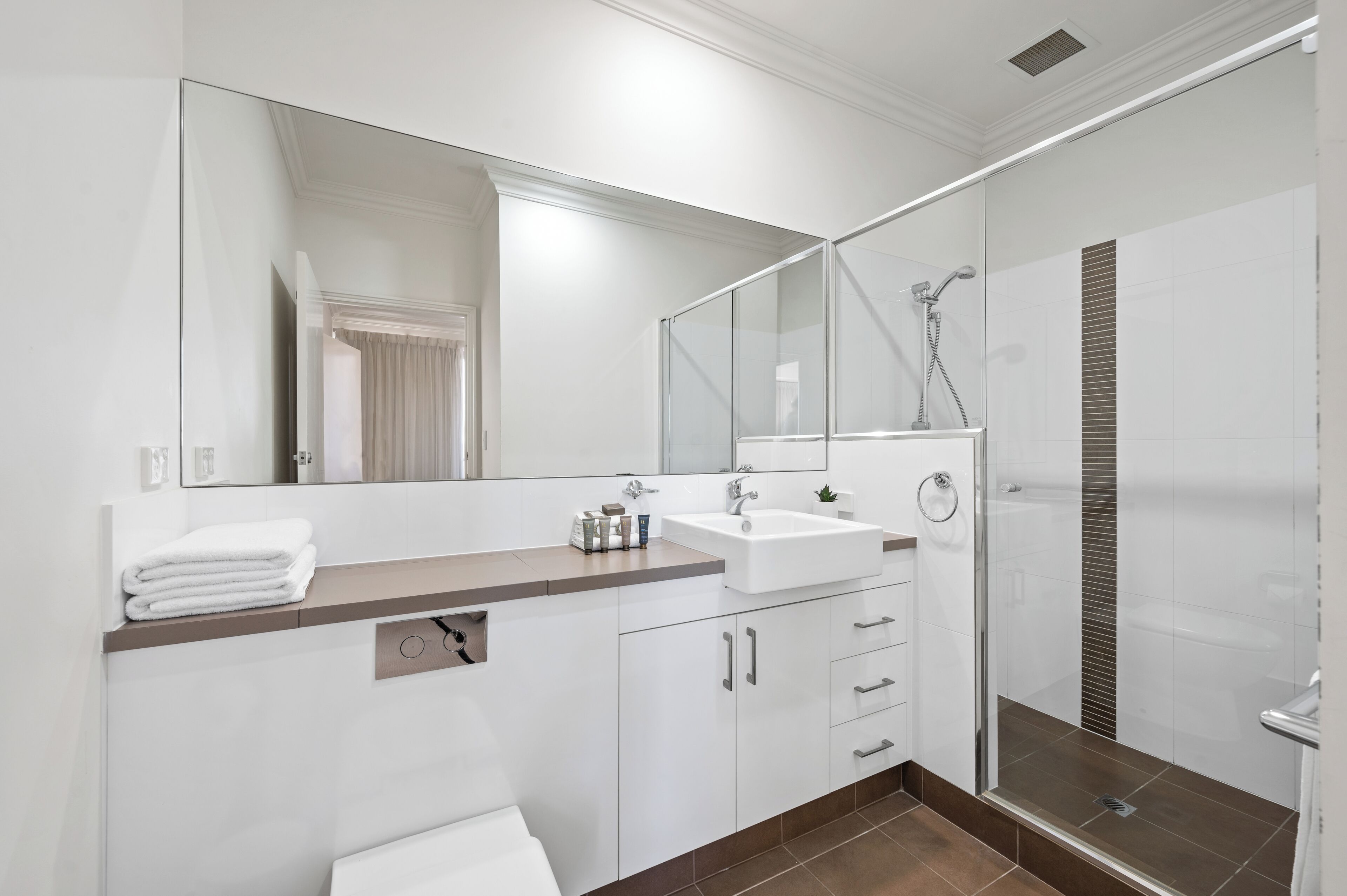 A modern bathroom with a large mirror, a sink, a shower, and a toilet.