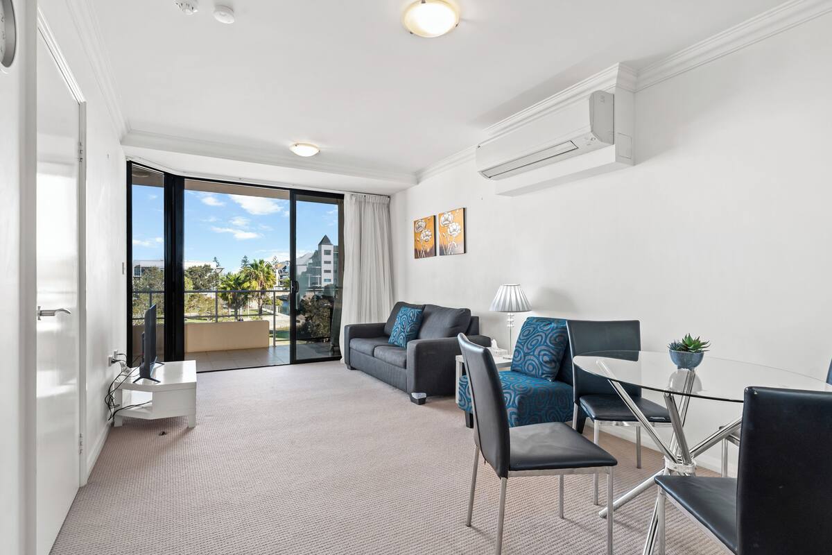 A modern hotel room with a balcony, a sofa, a dining table, and a TV.