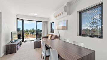 Una habitación moderna con una gran mesa de comedor, sillas blancas, un sofá y un televisor sobre un mueble bajo.