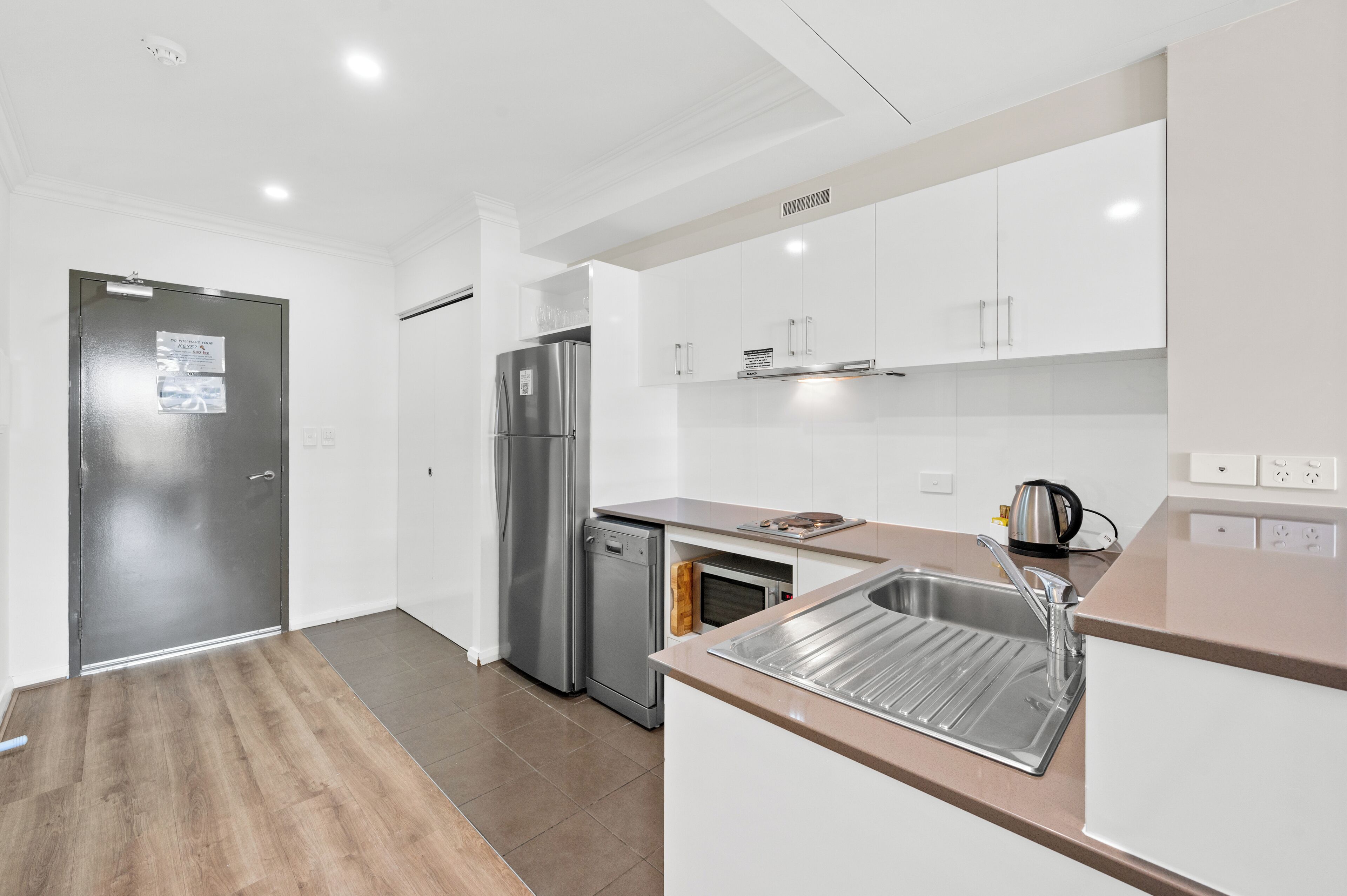A modern kitchen with white cabinets, stainless steel appliances, and a wooden floor.