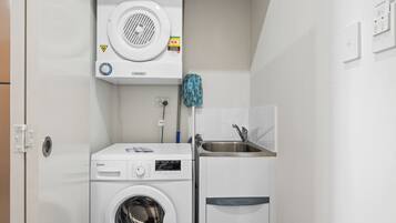 A compact laundry room with a front-loading washing machine, a dryer, and a sink.
