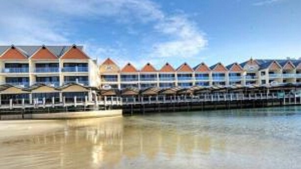 A beachfront hotel with multiple overwater bungalows, a sandy beach, and a clear blue sky. - Dolphin Quay Apartments (Mandurah)