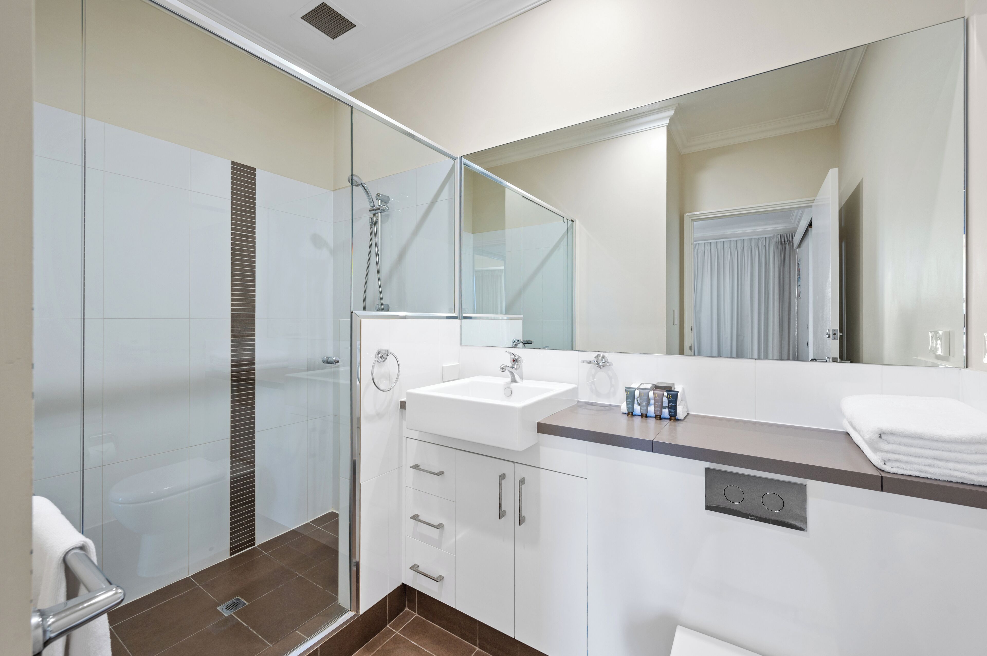 Une salle de bain moderne avec une douche à l’italienne en verre, un lavabo blanc et un grand miroir.