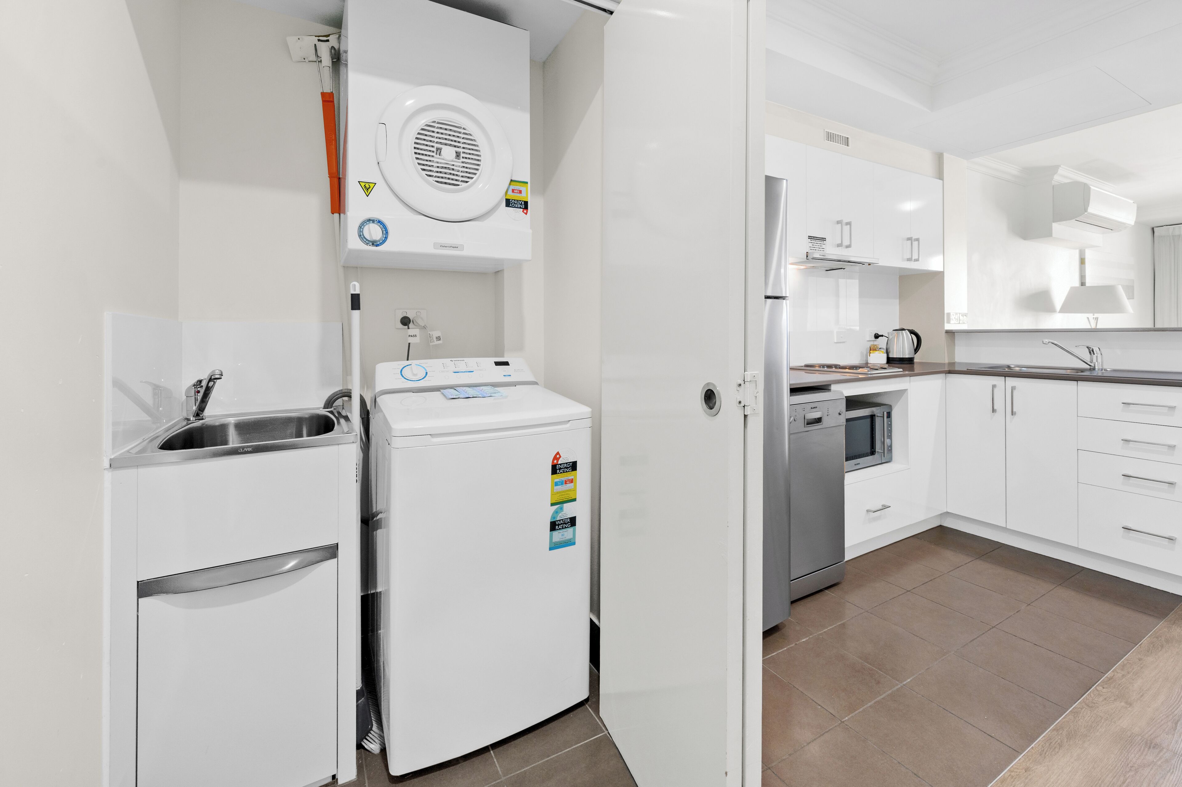 A modern kitchen with white cabinetry, a built-in oven, a microwave, and a stainless steel sink.