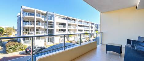 Un apartamento moderno con balcón, vistas a un edificio de varios pisos y un área de estar con mesa y sillas.