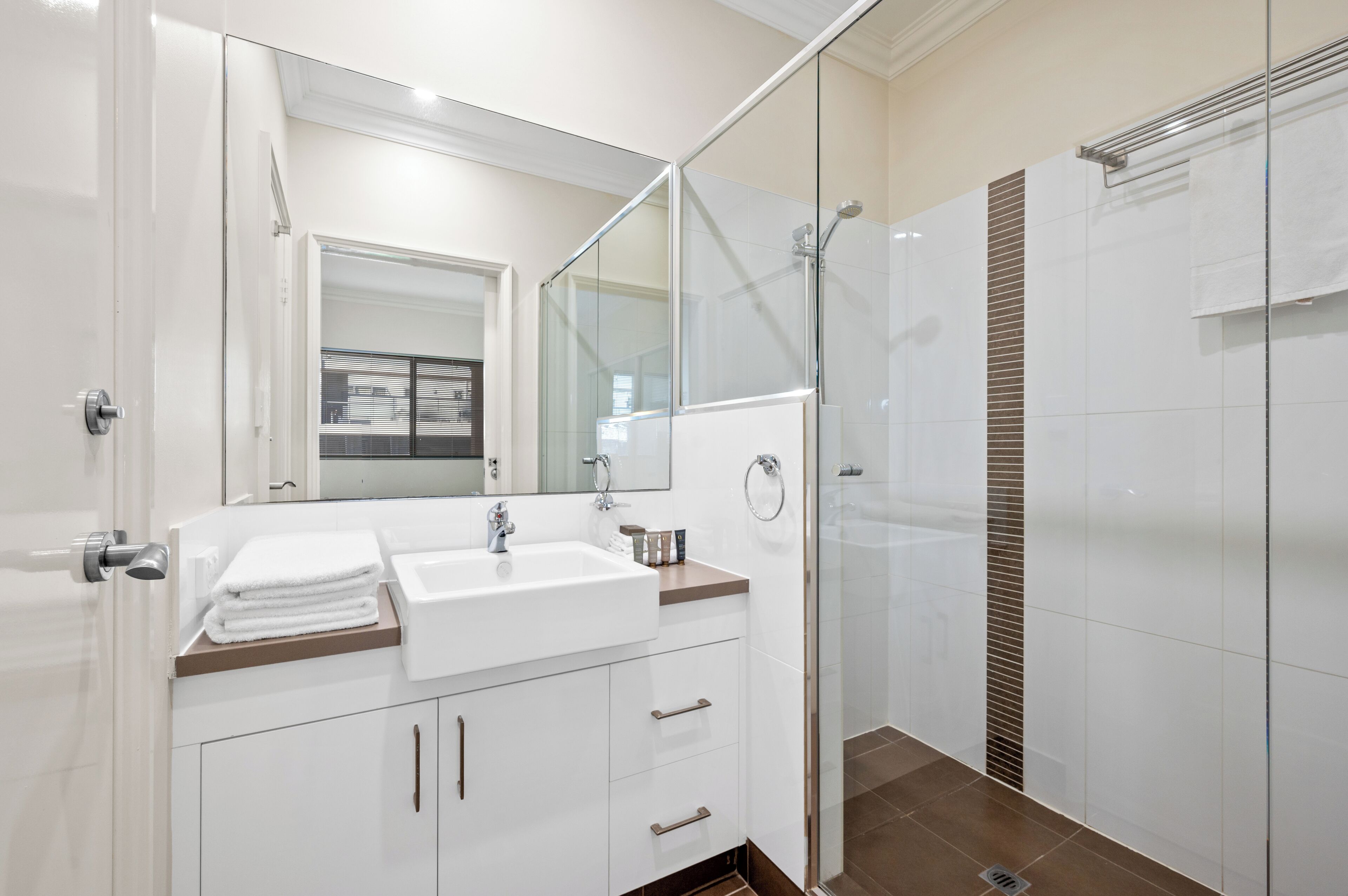 A modern bathroom with a glass shower enclosure, a white sink, and a large mirror.