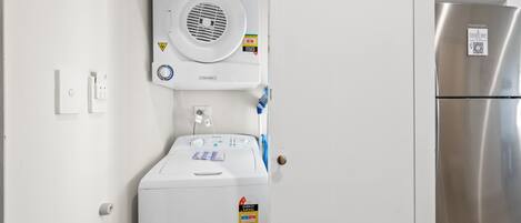 Cocina compacta con lavadora y secadora integradas, refrigerador de acero inoxidable y microondas sobre el horno.