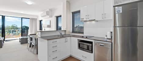 A modern kitchen with white cabinetry, stainless steel appliances, and a large window providing a view of the outdoors.