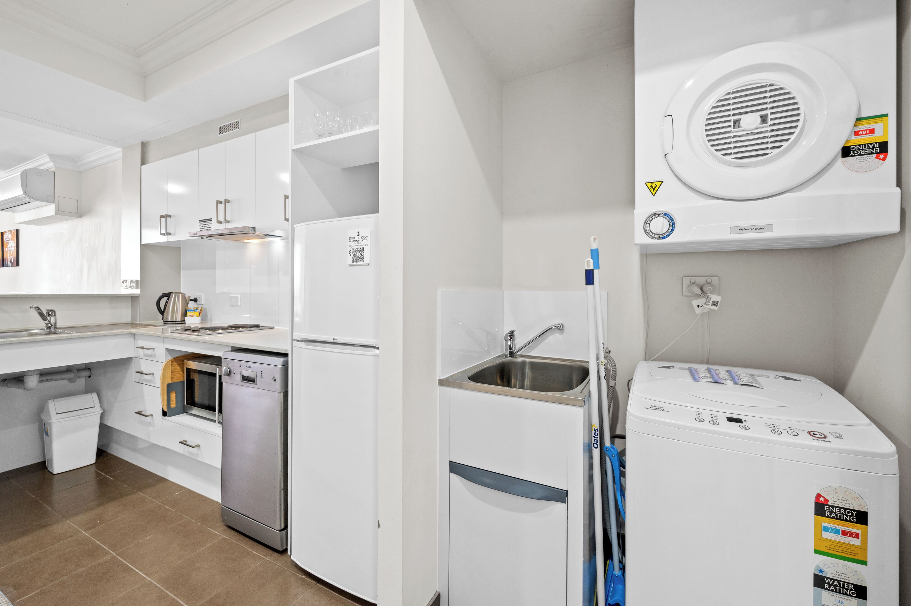 A modern kitchen with white cabinetry, a dishwasher, a built-in oven, and a washing machine.