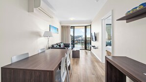 A modern hotel room with a dining area, a sofa, a TV, and a balcony with a city view. - Dolphin Quay Apartments (Mandurah)