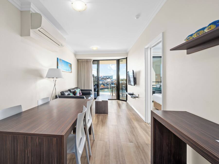 Una habitación de hotel moderna con zona de comedor, sofá, televisión y balcón con vistas a la ciudad.