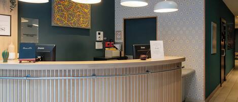 A reception desk with three pendant lights, a framed abstract painting, and a patterned wall.