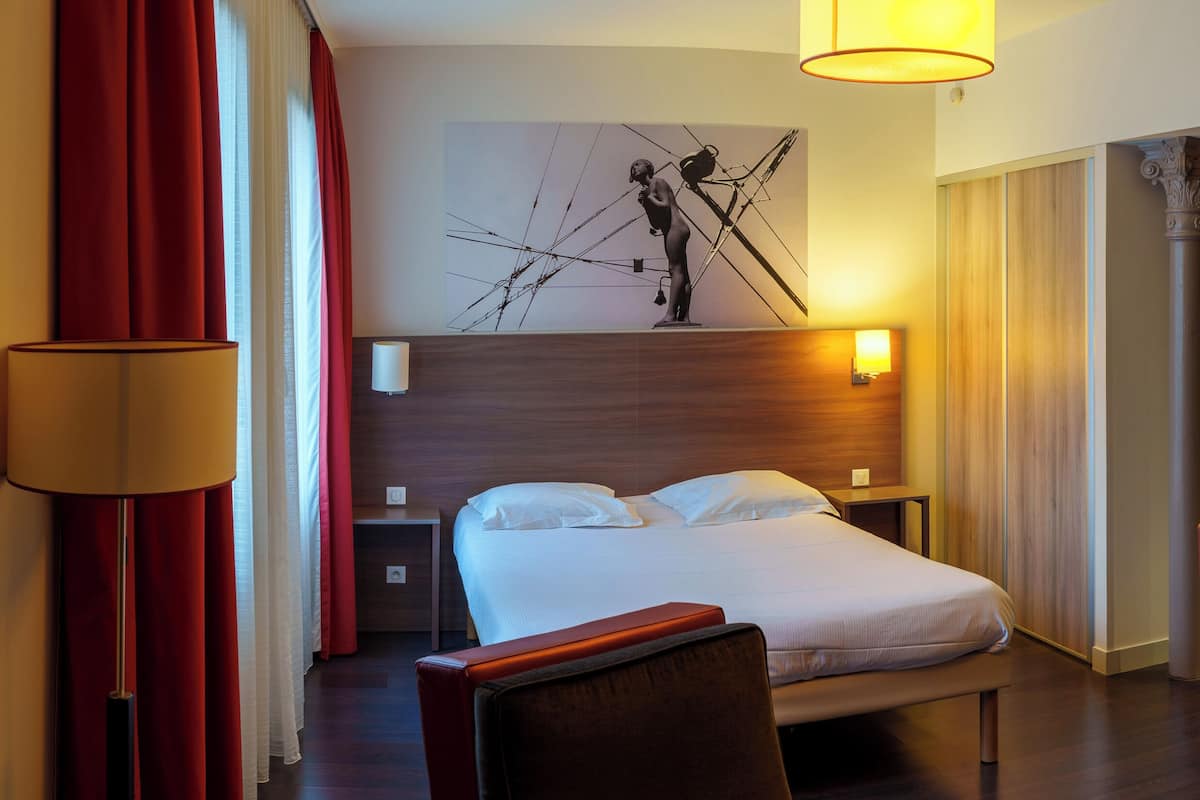 Una habitación de hotel con cama, mesita de noche, lámpara, una silla y una escultura en la pared.