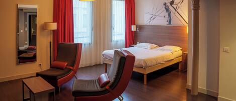 Una habitación de hotel con una cama, dos sillones, un escritorio, una lámpara y un cuadro en la pared.