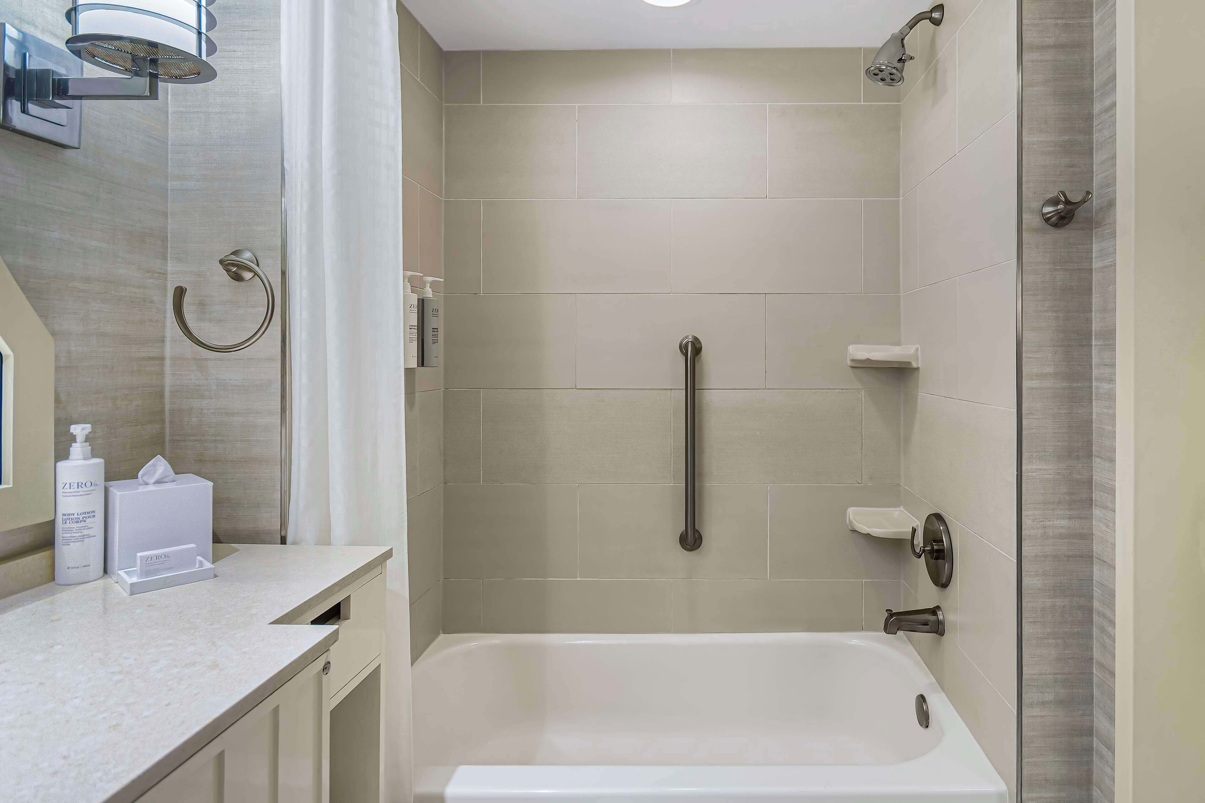 A modern bathroom with a bathtub, a shower with a handheld showerhead, a towel ring, and a soap dispenser on the counter.