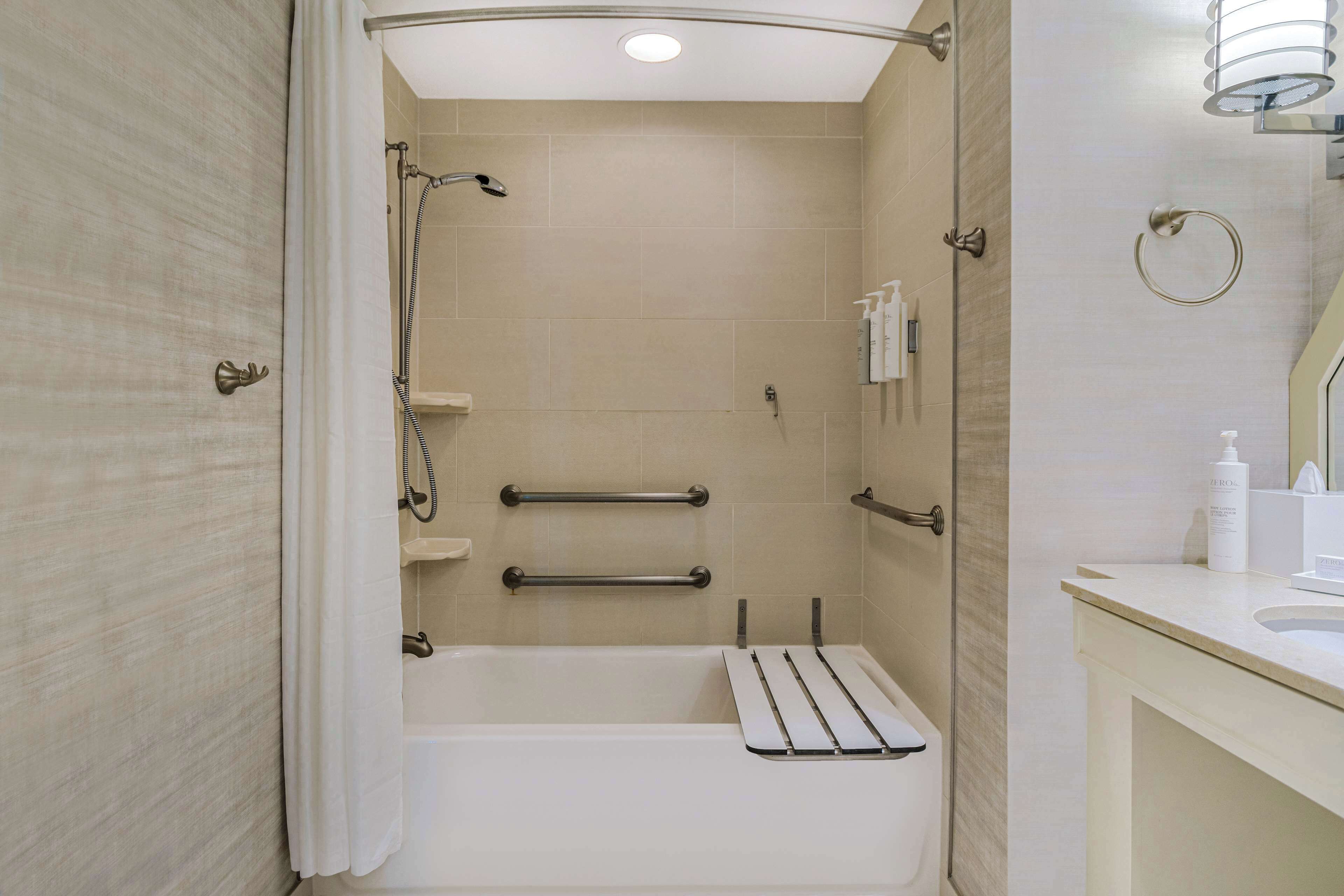 Un baño moderno con ducha a ras de suelo, barras de apoyo y tocador con espejo.