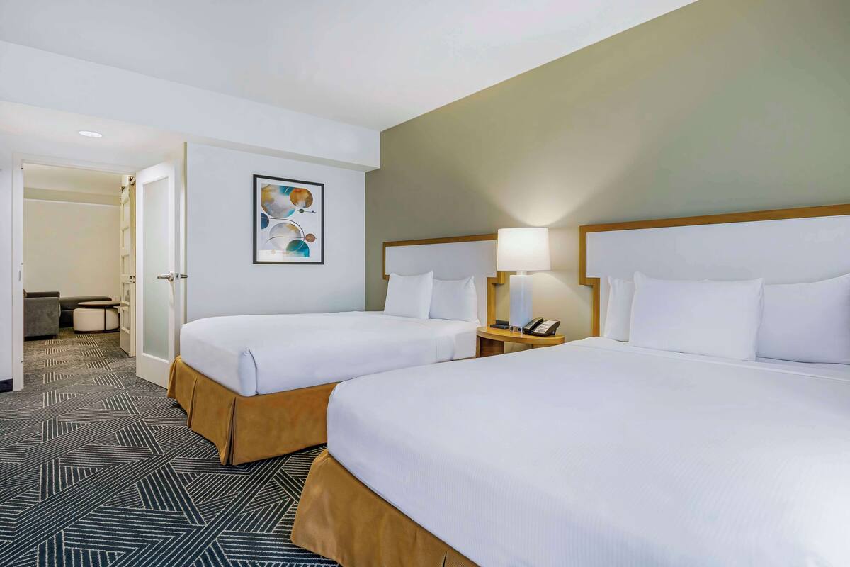A hotel room with two beds, a bedside table with a lamp, a small table with a phone, and a door leading to a bathroom.