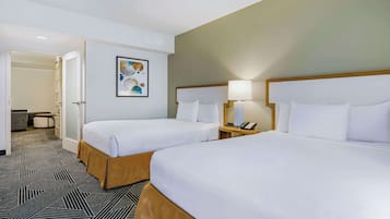 Habitación de hotel con dos camas, una mesita de noche con lámpara, una pequeña mesa con teléfono, y una puerta que da a un baño.
