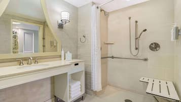A modern bathroom with a large mirror, two sinks, a shower with a grab bar, and a towel rack.