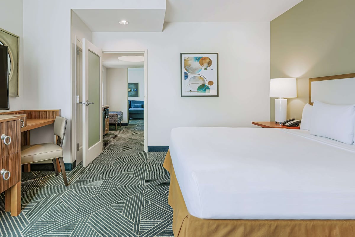 A hotel room with a bed, a desk, a chair, a lamp, and a painting on the wall.
