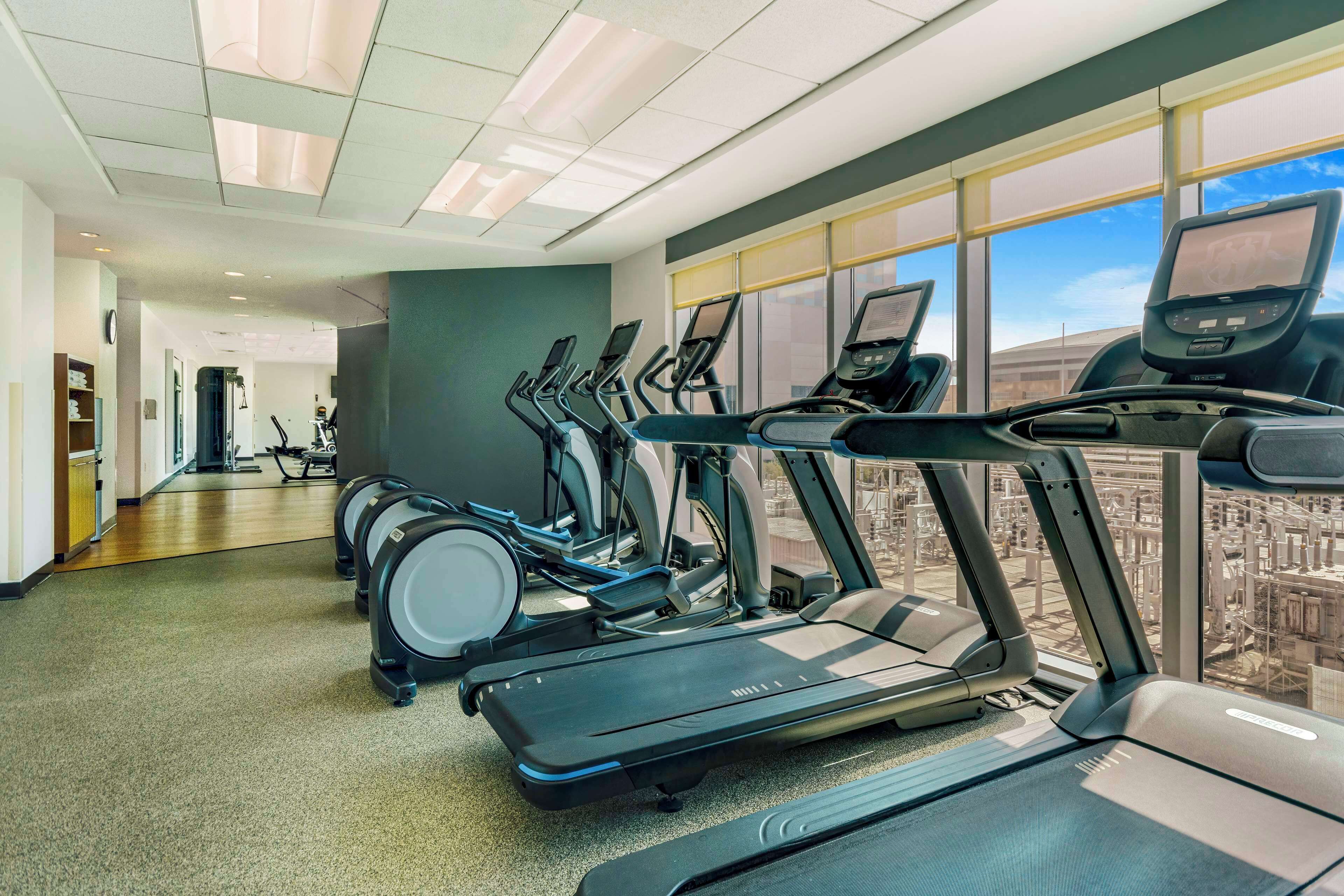 A gym with multiple treadmills, exercise bikes, and a large window with a city view.