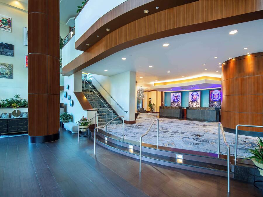 A spacious lobby with a central staircase, a reception desk, and a large plant.