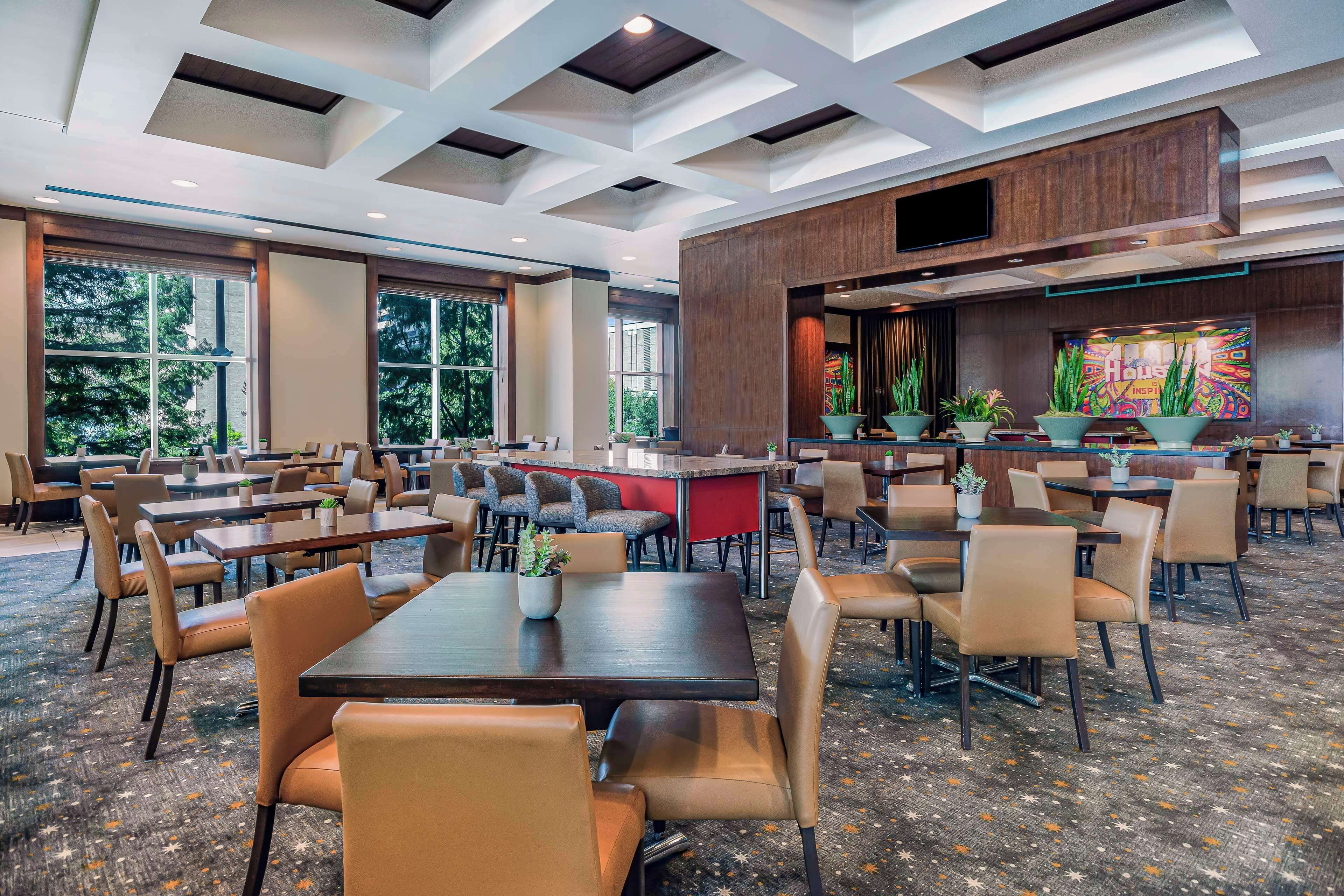 A spacious hotel lobby with multiple seating areas, large windows, and a modern ceiling design.