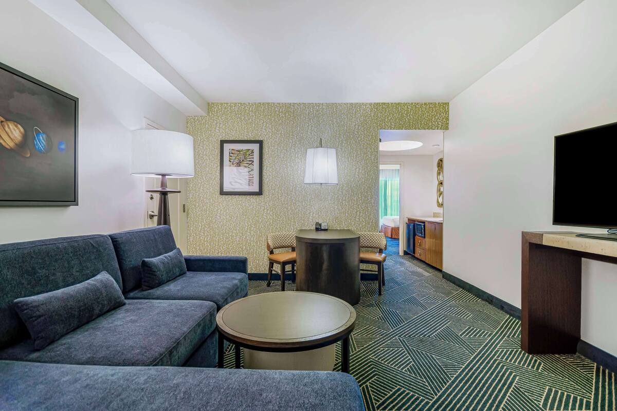 A hotel room with a sofa, a small round table, a TV, and a lamp.