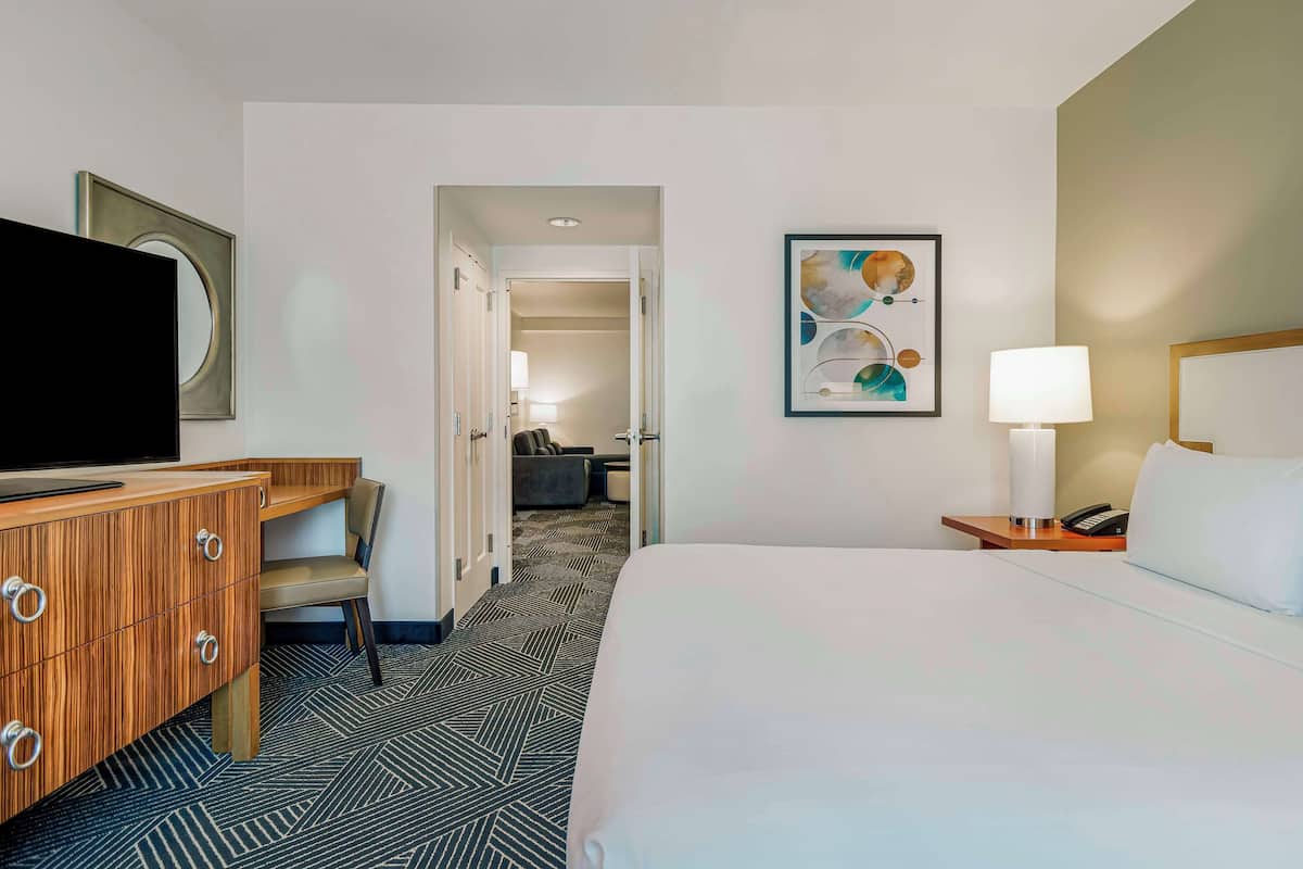 A hotel room with a bed, a desk with drawers, a television, a chair, a lamp, and a framed picture on the wall.