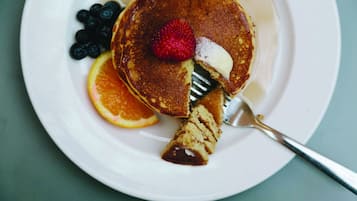 Lautasella on pannukakkuja, mansikka, mustikoita ja viipale appelsiinia.