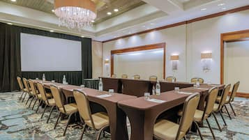 Un salón de conferencias con una pantalla grande, varias mesas y sillas, equipado con botellas de agua y tarjetas de identificación.