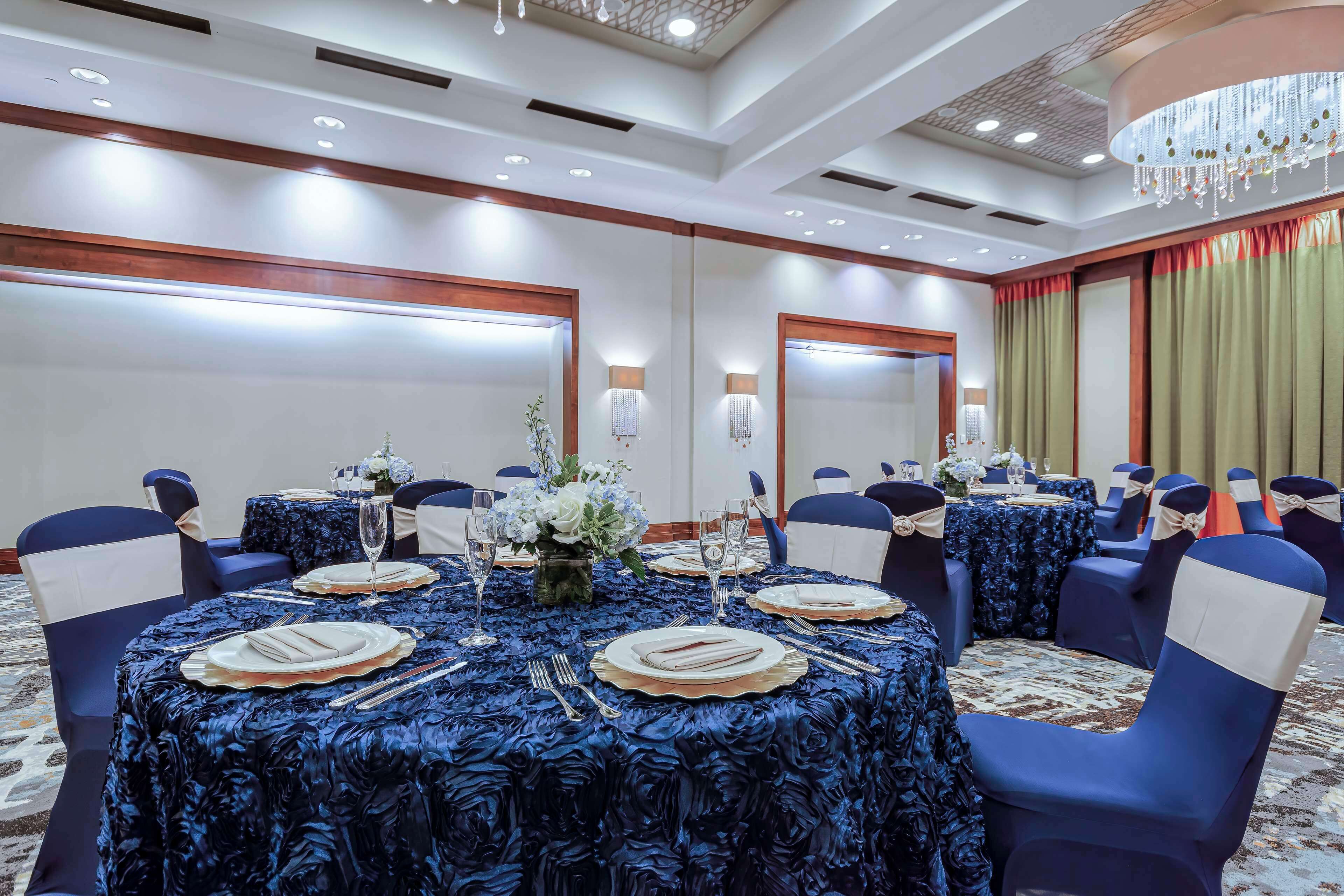 A banquet hall with round tables, blue chairs, and a chandelier.