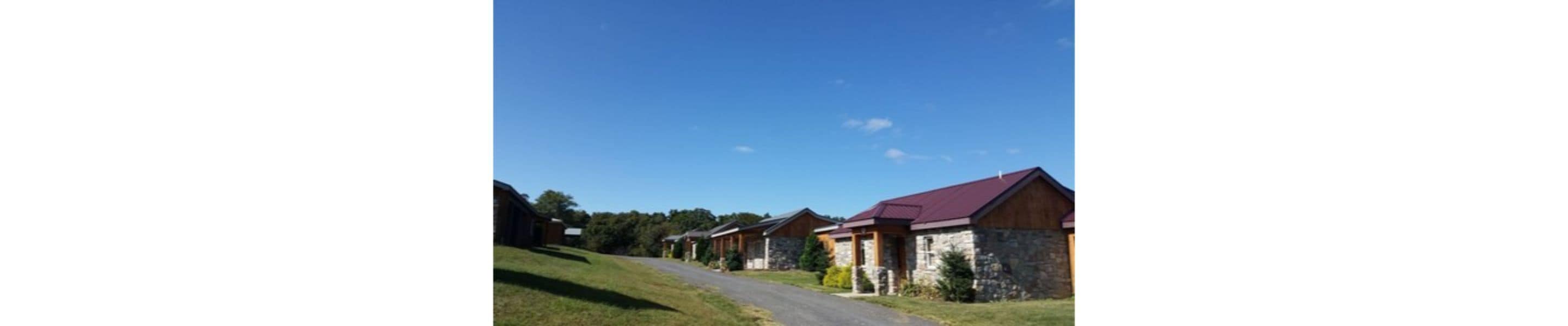 A row of stone buildings with red roofs, a paved road, and a clear blue sky.