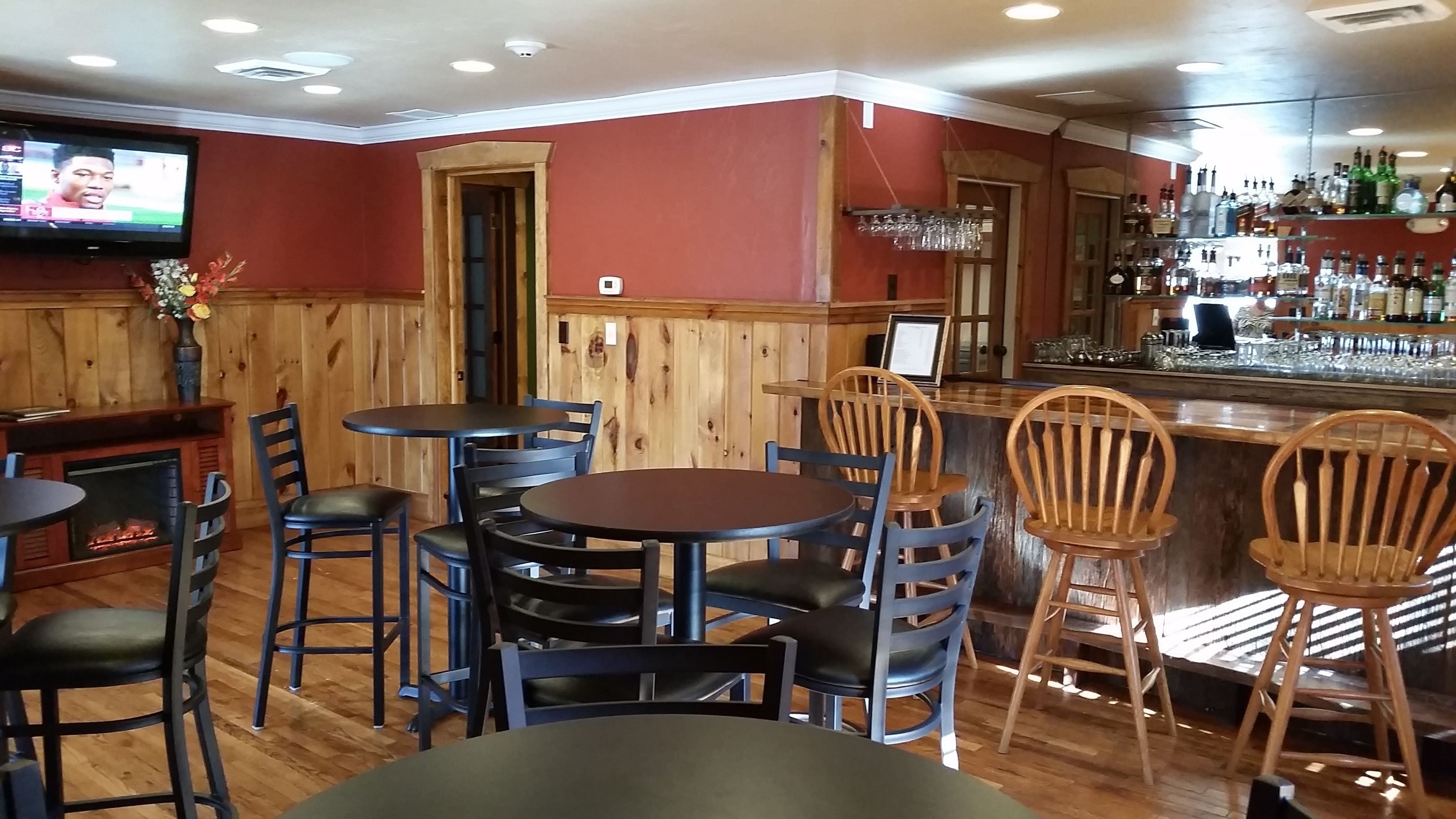 A bar area with wooden walls, a television mounted on the wall, and a variety of bar stools and tables.