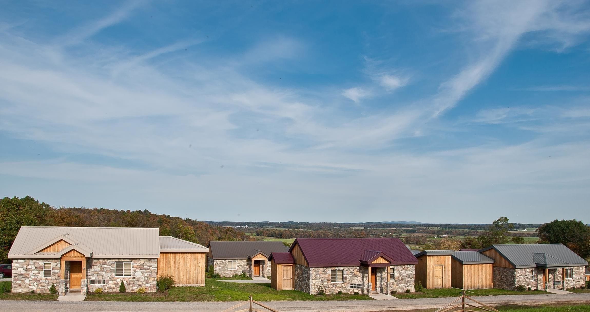 A row of cabins with stone and wooden exteriors, set against a rural backdrop.